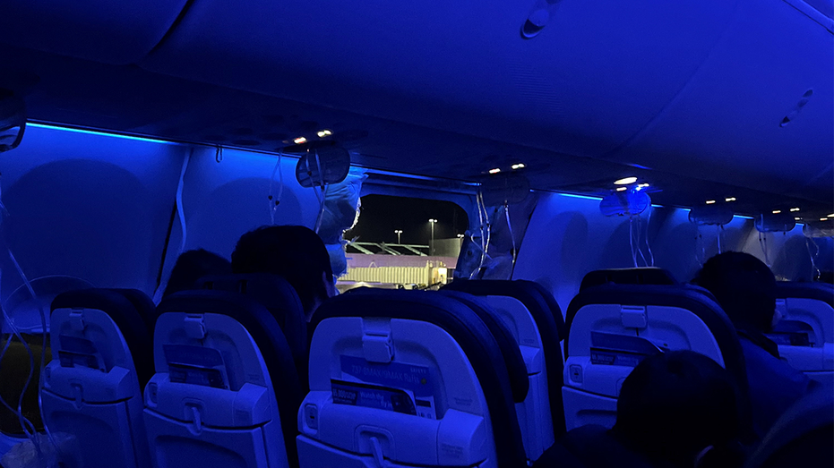 People sit on a plane next to a missing window and portion of a side wall of an Alaska Airlines Flight 1282.